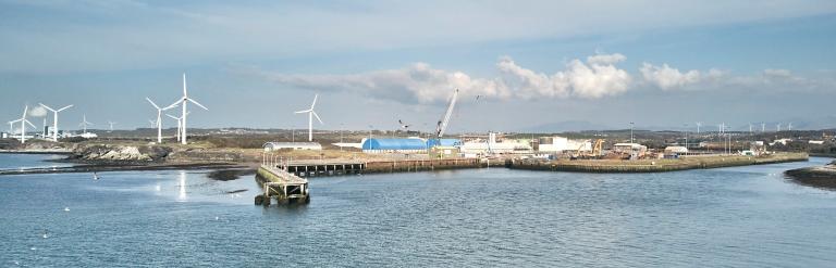 A view over the Port of Workington showing wind turbines, dockside cranes, industrial buildings, and harbour waters
